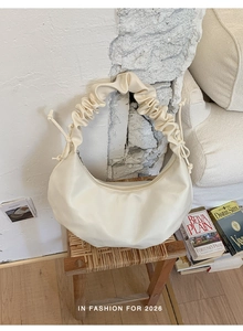 Detail of ruched handle and cream crescent bag on vintage wooden stool in soft light