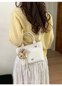 Elegant white bucket bag with bear pendant worn by model in a casual indoor setting