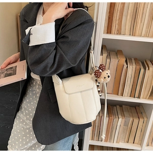 Detail of cream white bucket bag featuring elegant stitching and a cute bear charm