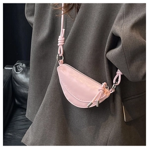Détail d'un mini sac bandoulière demi-lune rose avec nœud décoratif sur la sangle