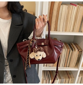 Détail du sac en similicuir bordeaux avec charm chien mignon et pompon rayé élégant