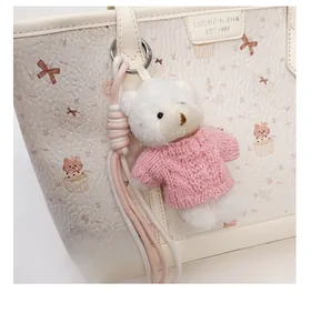 Dettaglio ravvicinato di un ciondolo a forma di orso bianco con maglione rosa sulla borsa