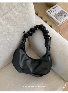 Detail of black pleated hobo bag with drawstring knots on a minimalist white sofa