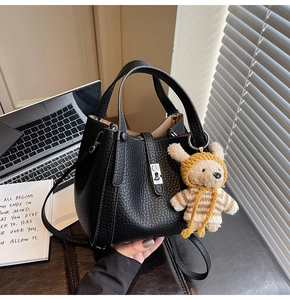 Gros plan d'un sac seau noir en cuir grainé avec un charm d'ours et un fermoir argenté