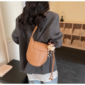 Detail of brown lychee grain shoulder bag with plush bear charm and beaded strap on model