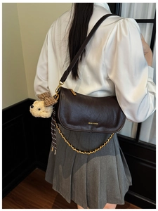 Detail of dark brown baguette bag featuring a gold chain and a plush teddy bear charm