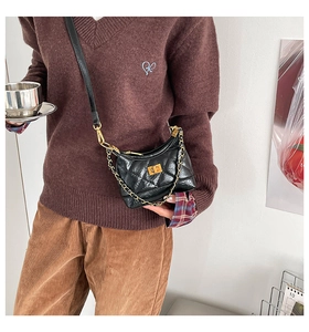 Detail of a black quilted crossbody bag with gold chain and metal twist lock closure