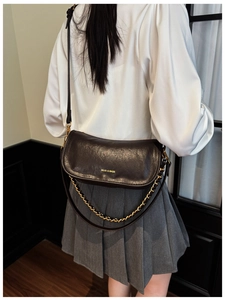 Detail of vintage dark leather baguette bag showing golden MUJU logo and metal chain strap