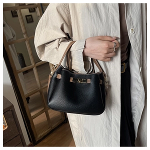 Détail du sac seau en cuir noir à grain de litchi avec fermoir doré et poignée marron