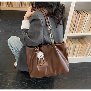 Detail of dark brown tote bag with metal chain strap and a white plush monster charm