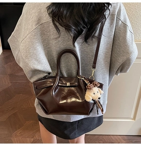 Détail du sac à main marron foncé brillant avec breloque chiot en peluche porté par modèle