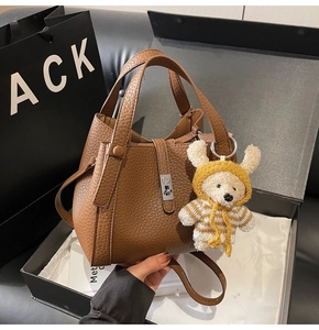 Détail d'un sac seau en cuir marron avec fermoir argenté et charm ours dans sa boîte cadeau