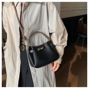 Détail du sac seau en cuir noir et marron avec fermoir doré sur un manteau beige