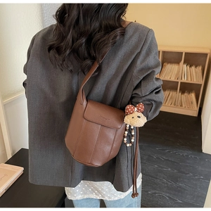 Brown lychee grain bucket bag with a cute teddy bear charm worn with a grey blazer