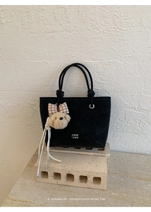 Close-up of black bucket bag with teddy bear charm and COIH 2DN logo on display