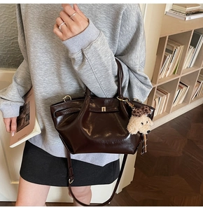 Détail d'un sac seau en cuir marron foncé brillant avec charm chiot en peluche blanc