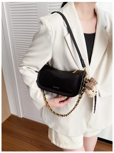 Detail shot of black leather baguette bag featuring a gold chain and cute teddy bear charm