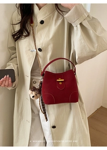 Détail du sac seau rouge avec fermoir doré et breloque ours sur un trench-coat beige chic