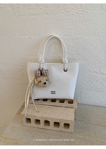 Detail of white minimalist handbag featuring GOIH 2DN logo and cute plush bear charm