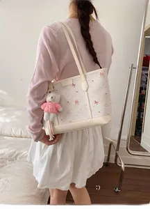 Dettaglio della borsa tote trapuntata crema con stampe cartoon e ciondolo a orsetto