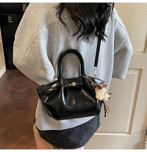 Détail d'un sac plissé en cuir brillant noir avec pendentif ours beige en peluche