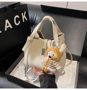 Gros plan du sac seau en cuir blanc cassé grainé avec fermoir argenté et breloque peluche
