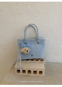 Detail view of light blue suede tote bag with bear charm and retro printed lettering