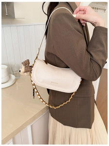Detail of cream crescent shoulder bag with gold chain strap and teddy bear charm