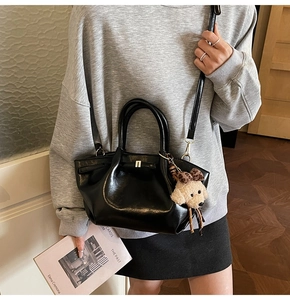 Gros plan d'un sac à main noir brillant avec breloque chiot et bandoulière réglable