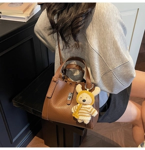 Détail d'un sac seau marron avec motif litchi, fermoir argenté et charm ours en peluche