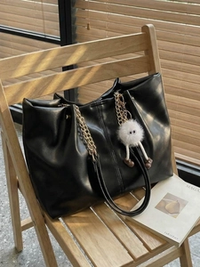 Large black tote bag with chain straps and plush monster charm on a wooden chair
