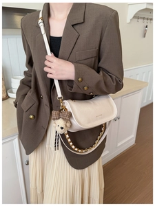 Detail of a creamy leather shoulder bag with metal chain and a cute teddy bear charm