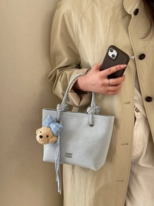 Light blue bucket bag with rope knot handles and a cute bear charm in minimalist setting