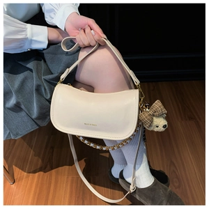 Detail of beige crescent bag with gold chain, PU leather texture, and cute bear charm