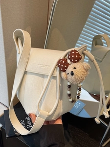 Chic beige leather bucket bag with plush bear charm and pebbled texture for women