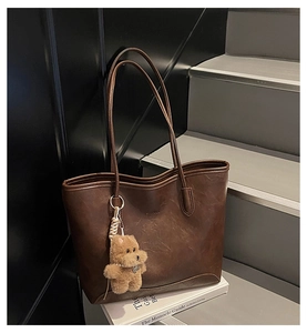 Detalle de primer plano del bolso tote de cuero PU marrón con un colgante de oso de peluche