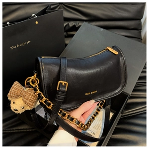 Detailed macro view of the black leather baguette bag featuring a gold chain and bear charm