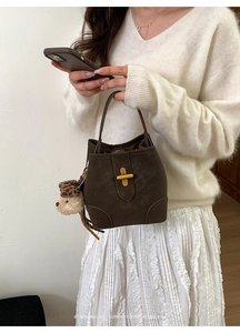 Détail d'un sac seau en daim marron avec fermoir doré en croix et charm de chien en peluche