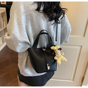 Detail of black lychee grain leather bucket bag with silver lock and puppy charm