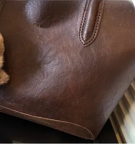 Detalle de bolso tote de cuero PU marrón con logo dorado y llavero de oso de peluche