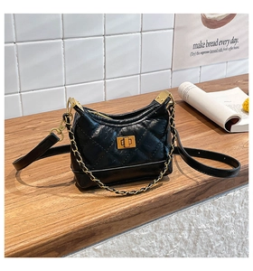 Close-up of black quilted leather shoulder bag with gold hardware on wooden surface