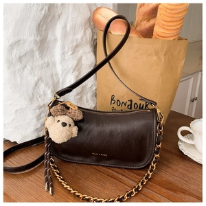 Detail of a dark brown vintage baguette bag with gold chain and a plush teddy bear charm