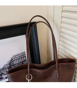 Detalle de bolso tote marrón oscuro vintage con textura de cuero y correas de hombro finas