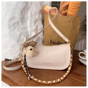 Chic beige baguette bag with gold chain strap and plush puppy charm on wooden table