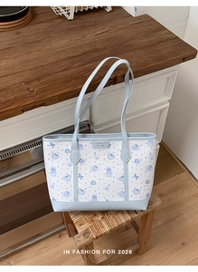Dettaglio della borsa tote blu e bianca con stampe di gatti su uno sgabello di legno