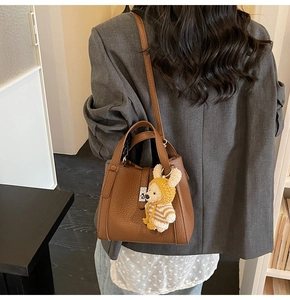 Sac seau marron avec texture litchi et charme d'ours porté par un mannequin stylé