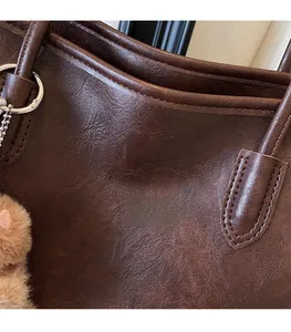 Primer plano del bolso tote marrón oscuro mostrando textura de cuero y logo dorado grabado