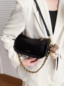 Elegant black crescent baguette bag with gold chain and plush bear charm on a model