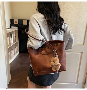 Detalle del bolso tote marrón oscuro con textura de cuero y un lindo colgante de oso