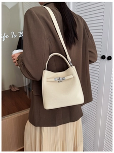 Chic beige leather bucket bag with silver lock worn by a model in a modern urban style